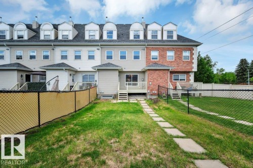 Rear exterior featuring a grass lawn, chain-link fencing, and a stone paver pathway - 14 4367 Veterans Way, Edmonton, AB 