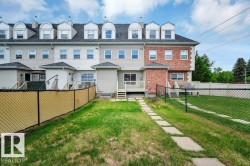 Rear exterior featuring a grass lawn, chain-link fencing, and a stone paver pathway - 