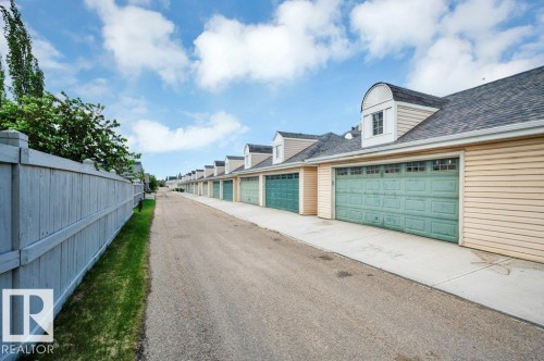 Row of garages featuring overhead doors with upper window panels, light-colored siding, and dormer windows - 14 4367 Veterans Way, Edmonton, AB 