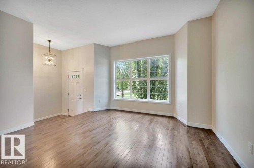 Expansive room featuring wood-finish flooring and a large window with multiple panes - 14 4367 Veterans Way, Edmonton, AB 