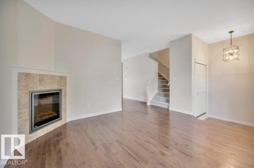Warm wood-finish flooring complements the corner-mounted fireplace with a tiled surround - 14 4367 Veterans Way, Edmonton, AB 