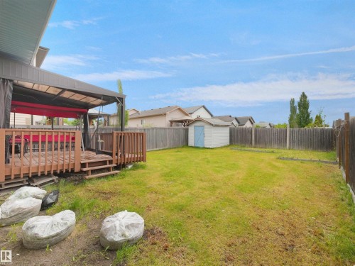 Expansive backyard featuring a wood deck with a covered pergola, a storage shed, a wood fence, and a generous lawn area - 2418 32B Street, Edmonton, AB 