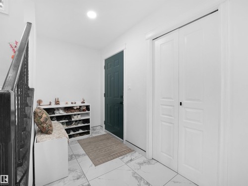 Entryway featuring white tile flooring with gray veining, a dark panel door, and white bi-fold closet doors - 2418 32B Street, Edmonton, AB 