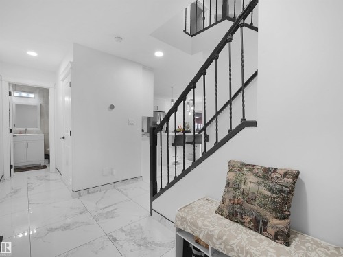 Entryway featuring large format marble-look tile flooring and a black wrought iron staircase railing - 2418 32B Street, Edmonton, AB 