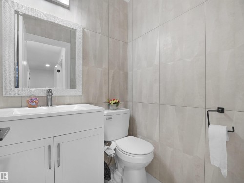 Modern bathroom featuring a white vanity with integrated sink, rectangular framed mirror, and large format wall tiling - 2418 32B Street, Edmonton, AB 