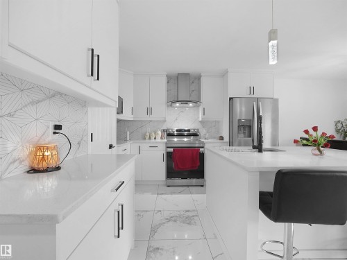 Modern kitchen featuring white cabinetry with dark hardware, stainless steel appliances, and a marble-patterned backsplash - 2418 32B Street, Edmonton, AB 