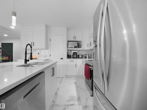 Modern kitchen featuring white cabinetry, a large kitchen island with an undermount sink, stainless steel appliances, and large format floor tiling - 2418 32B Street, Edmonton, AB 