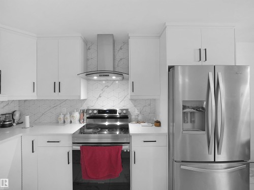 Modern kitchen featuring white cabinetry with black hardware, a stainless steel range with a coordinating vent hood, a stainless steel French door refrigerator, and a geometric tiled backsplash - 2418 32B Street, Edmonton, AB 