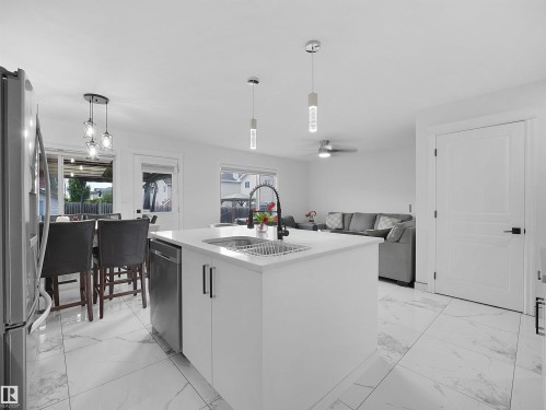Modern kitchen island featuring a stainless steel sink with a matte black faucet, integrated dishwasher, and white cabinetry - 2418 32B Street, Edmonton, AB 
