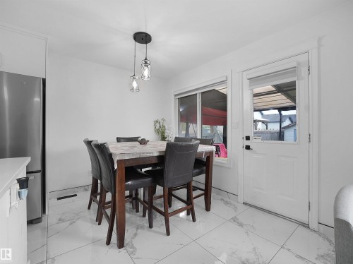 Dining area featuring a stainless steel refrigerator, white walls, white trim, a built-in window, a door with a window pane, and large format white tile flooring with gray veining - 2418 32B Street, Edmonton, AB 