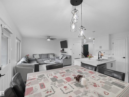 Open-concept living space featuring a modern kitchen island with seating, pendant lighting, white cabinetry, and a black faucet - 2418 32B Street, Edmonton, AB 