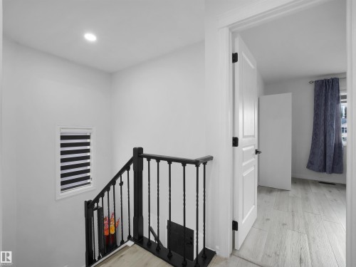 Staircase with black wrought iron balusters, light wood-finish flooring, and recessed lighting - 2418 32B Street, Edmonton, AB 