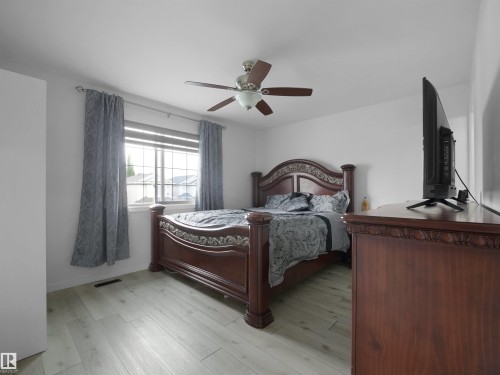 Spacious room featuring light wood-finish flooring, a ceiling fan with light fixture, and a large window with white framing - 2418 32B Street, Edmonton, AB 