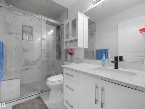 Full bathroom featuring a white vanity with integrated sink, speckled countertop, and black faucet - 2418 32B Street, Edmonton, AB 