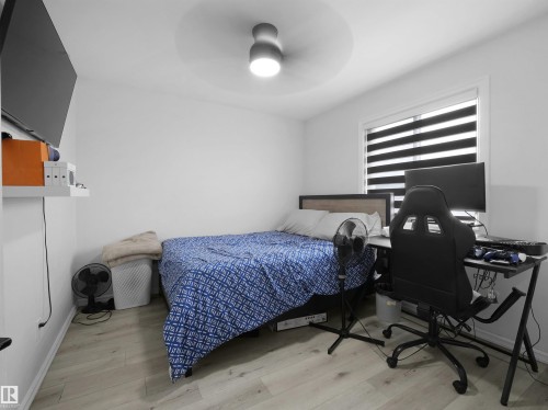 Room featuring light-toned wood-finish flooring, a ceiling-mounted light fixture, a window with horizontal blinds, and a wall-mounted shelf - 2418 32B Street, Edmonton, AB 