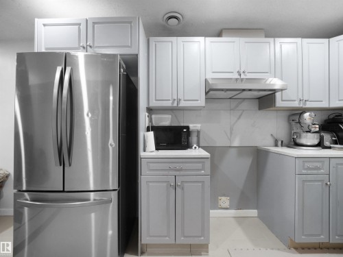 Contemporary kitchen featuring two-tone cabinetry, stainless steel appliances, a range hood, and a tiled backsplash - 2418 32B Street, Edmonton, AB 