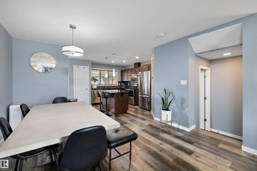 Open-concept living space featuring wood-finish flooring, a kitchen island with seating, dark wood cabinetry, and stainless steel appliances - 2833 Chokecherry Place, Edmonton, AB 