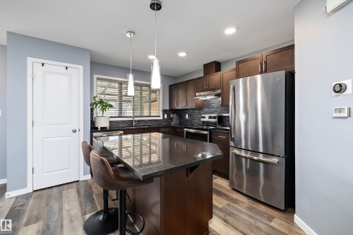 Kitchen featuring a dark granite island, dark wood-finish cabinetry, stainless steel appliances, and wood-finish flooring - 2833 Chokecherry Place, Edmonton, AB 