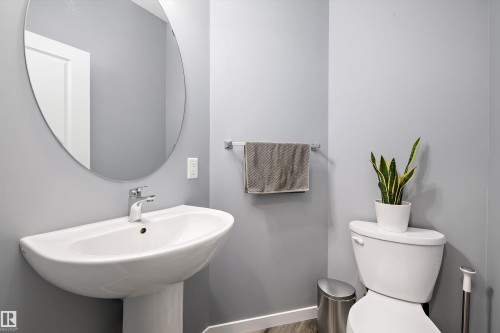 Pedestal sink with chrome fixtures, a circular frameless mirror, and light gray wall paint - 2833 Chokecherry Place, Edmonton, AB 