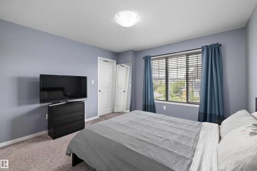Spacious room featuring light blue walls, two white panel doors, and a large window with horizontal blinds and blue fabric curtains - 2833 Chokecherry Place, Edmonton, AB 