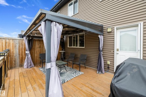Wood-finish deck featuring a metal-frame gazebo with privacy curtains, vertical wood fencing, and horizontal siding on the structure - 2833 Chokecherry Place, Edmonton, AB 