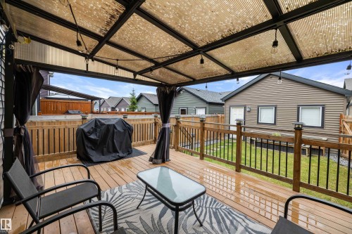 Expansive wood-finish deck featuring a translucent overhead canopy, string lighting, and black privacy curtains - 2833 Chokecherry Place, Edmonton, AB 