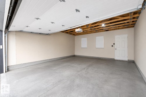 Spacious garage featuring a concrete floor, light-toned walls, overhead lighting, an exposed ceiling with wooden beams, and a white paneled entry door - 2833 Chokecherry Place, Edmonton, AB 