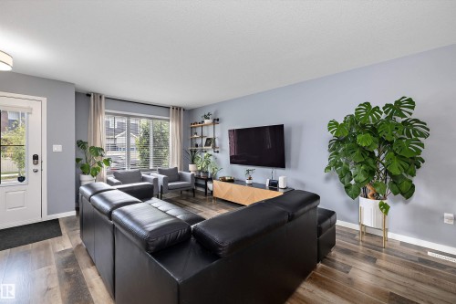 Inviting living area featuring wood-finish flooring, a bright window with blinds, and a built-in wall shelf - 2833 Chokecherry Place, Edmonton, AB 