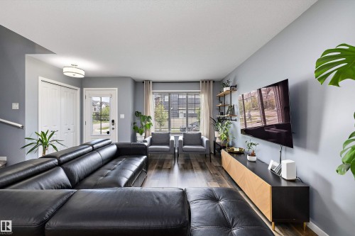 Open-concept living space with wood-finish flooring, a contemporary ceiling light fixture, and a front entry door with integrated window panels - 2833 Chokecherry Place, Edmonton, AB 