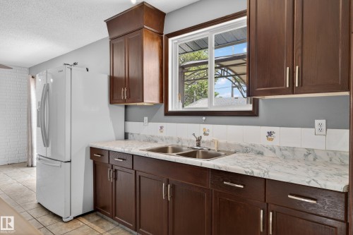 Kitchen featuring wood-finish cabinetry, a double basin stainless steel sink, and a window with wood trim - 13427 114 Street, Edmonton, AB 