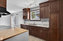 Kitchen featuring dark wood-finish cabinetry, light-toned countertops, a stainless steel double-basin sink, and a white tiled backsplash - 