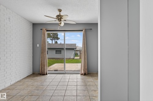 Spacious interior room featuring tile flooring, a white brick accent wall, and a ceiling fan - 13427 114 Street, Edmonton, AB 