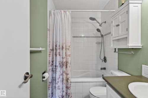 Bathroom featuring a white tiled tub/shower combination with a decorative accent band and dual shower heads - 13427 114 Street, Edmonton, AB 