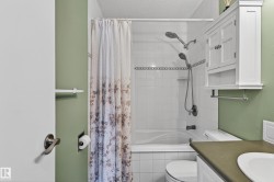 Bathroom featuring a white tiled tub/shower combination with a decorative accent band and dual shower heads - 