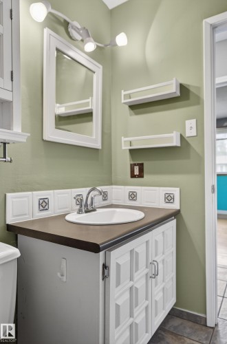 Bathroom vanity featuring a drop-in sink, chrome fixtures, and white paneled cabinetry - 13427 114 Street, Edmonton, AB 