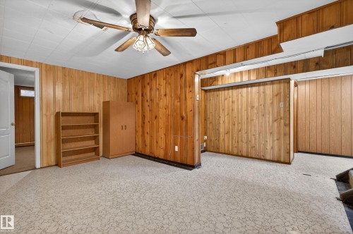 Carpeted room featuring wood paneling, a white ceiling with acoustic tiles, and a ceiling fan with light fixture - 13427 114 Street, Edmonton, AB 