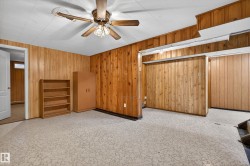 Carpeted room featuring wood paneling, a white ceiling with acoustic tiles, and a ceiling fan with light fixture - 