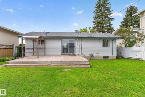Rear exterior featuring a spacious wood deck, sliding glass door, and a manicured lawn - 13427 114 Street, Edmonton, AB 