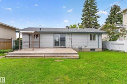 Rear exterior featuring a spacious wood deck, sliding glass door, and a manicured lawn - 