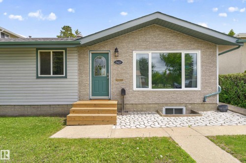 Exterior featuring a teal entry door with decorative glass, new wood steps, a large picture window, and textured stone-look siding - 13427 114 Street, Edmonton, AB 