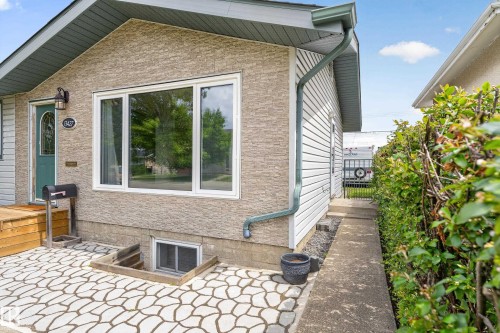 Front exterior featuring textured siding, white framed windows, and a teal entry door - 13427 114 Street, Edmonton, AB 