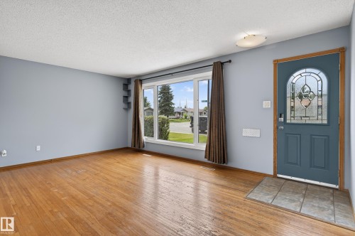 Spacious room featuring wood-finish flooring, a large picture window, and a decorative stained-glass entry door - 13427 114 Street, Edmonton, AB 