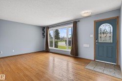 Spacious room featuring wood-finish flooring, a large picture window, and a decorative stained-glass entry door - 