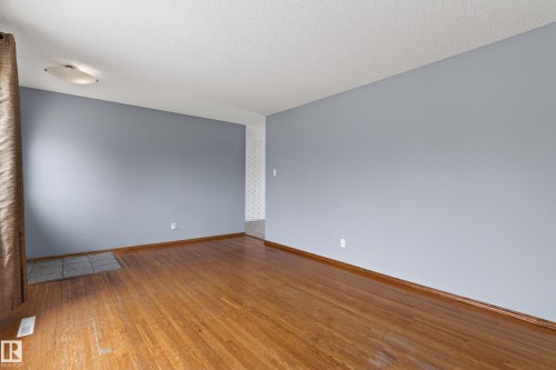 Spacious room featuring wood-finish flooring, light blue painted walls, and white baseboards - 13427 114 Street, Edmonton, AB 
