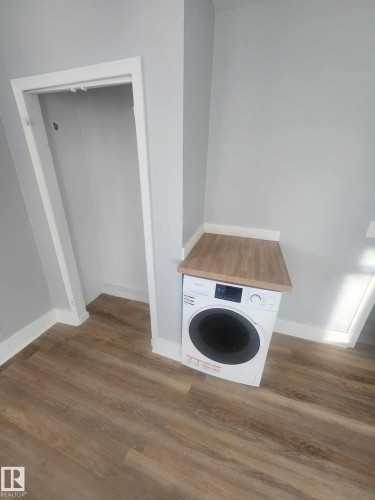 Dedicated laundry area featuring a front-load appliance, wood-finish countertop, light gray walls, white trim, and wood-finish flooring - 11308 94 Street, Edmonton, AB 