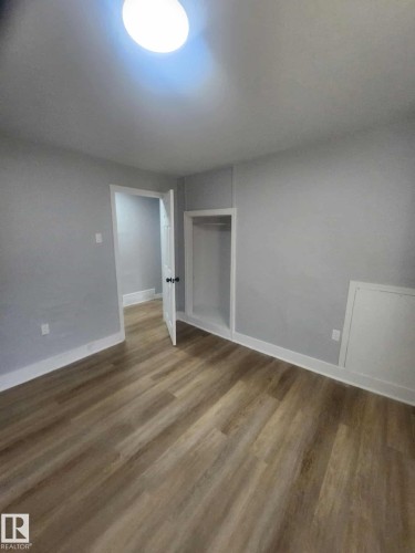 Room with wood-finish flooring, light gray walls, white trim, a flush-mount ceiling light fixture, and an open closet - 11308 94 Street, Edmonton, AB 