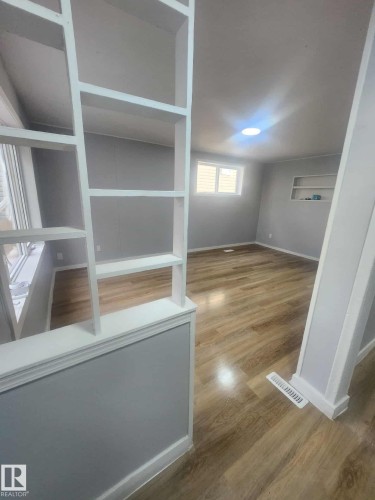 Open-concept interior featuring wood-finish flooring, light gray walls, built-in shelving, and a recessed ceiling light fixture - 11308 94 Street, Edmonton, AB 