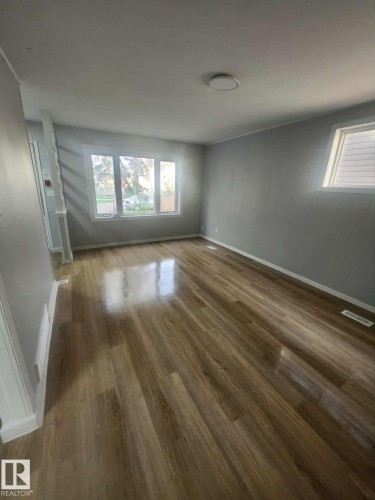 Spacious interior room featuring wood-finish flooring, light gray wall paint, white baseboards, and a contemporary ceiling light fixture - 11308 94 Street, Edmonton, AB 