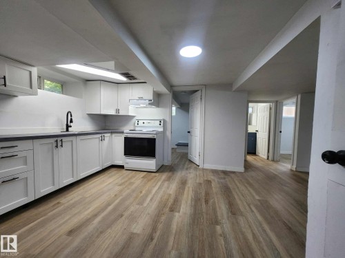 Kitchen space featuring wood-finish flooring, white cabinetry with matte black hardware, a black kitchen faucet, and dark countertops - 11308 94 Street, Edmonton, AB 