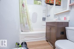 Bathroom featuring a white bathtub, wood-finish flooring, and a vanity with a white countertop and brown cabinetry - 